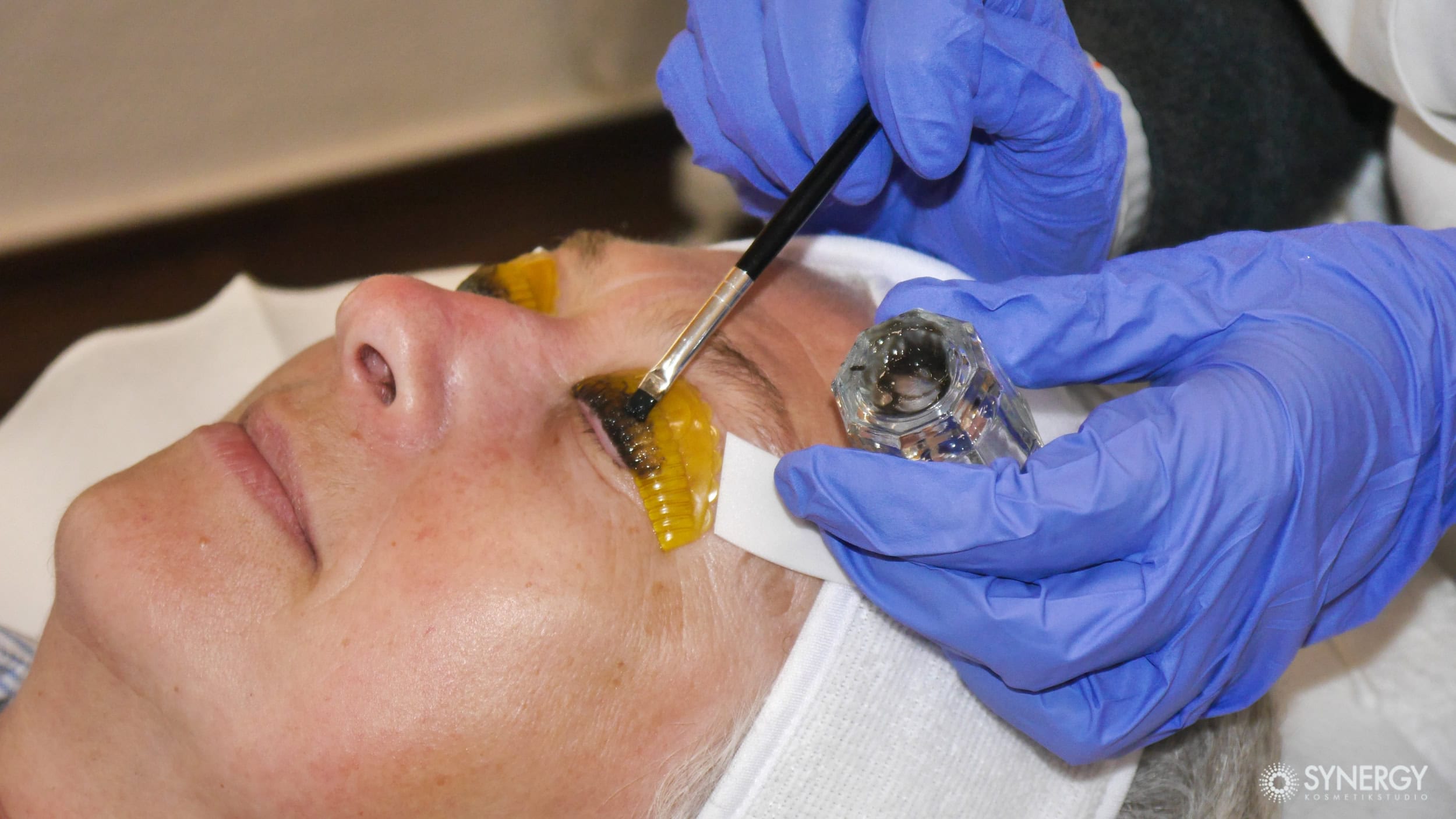 A woman getting her eyes done with a yellow eye liner.